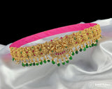 Gold necklace with green and red stones on a white fabric background