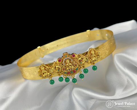 Gold bracelet with green and red gemstones on a white satin background