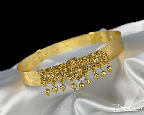 Gold bracelet with intricate design and dangling beads on a white fabric background