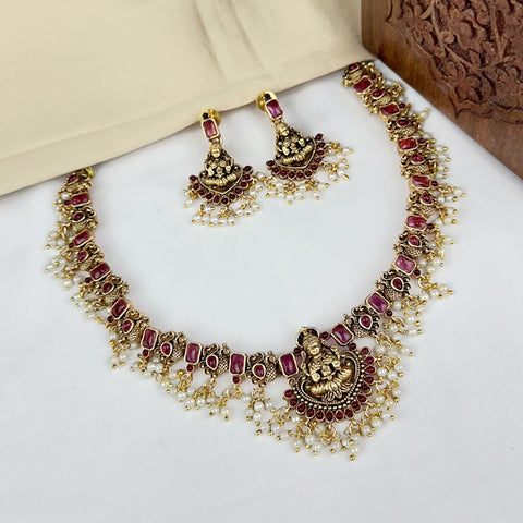 Gold necklace with red stones and matching earrings on a white surface