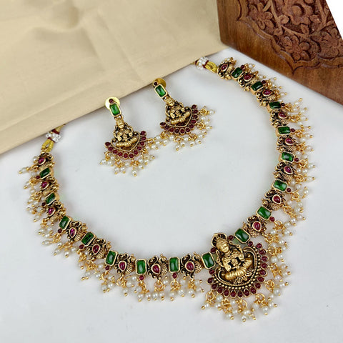 Gold necklace with green and red stones and matching earrings on a white surface.