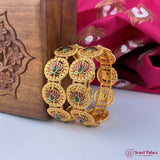 Gold bangles with floral designs on a wooden box and pink fabric background