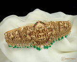 Gold and green beaded jewelry piece on a white fabric background