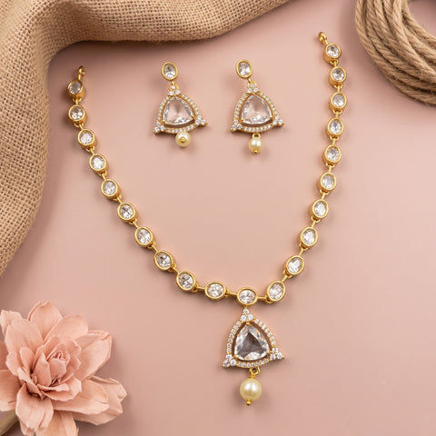 Gold-toned traditional jewelry set featuring a necklace, matching earrings, and a waist chain with clear stones and pearl-like drops, arranged on a soft pink background with decorative burlap and a pink flower.