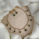 Gold necklace with green gemstones on a beige stand against a white fabric background