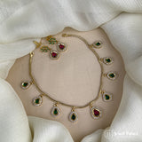 Gold necklace with green and red gemstones on a beige stand with a white fabric background
