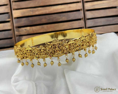 Gold necklace with intricate design and hanging beads on a white cushion with wooden background