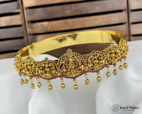 Gold crown with intricate designs and dangling beads on a mannequin head against a wooden background.