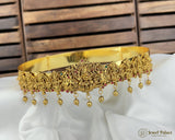 Gold necklace with intricate design and dangling beads on a white fabric background
