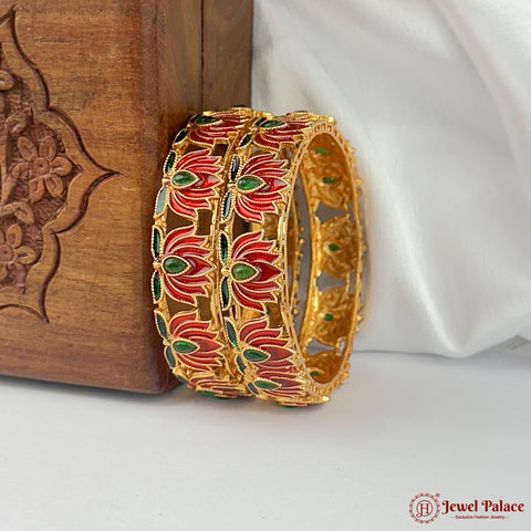Decorative gold bangle with red and green floral patterns on a white surface with a wooden box in the background.
