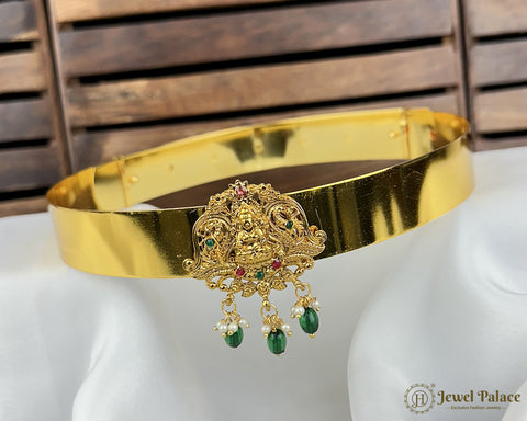 Gold headband with intricate design and green gemstones on a white stand with wooden background