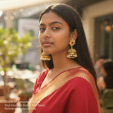 Woman wearing a red saree with gold border and large earrings outdoors.