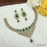 Jewelry set with necklace and earrings featuring green gemstones on a white fabric background.