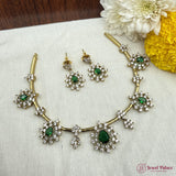 Gold necklace with green gemstones and matching earrings on a white fabric background with flowers.