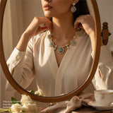 Woman wearing a necklace and earrings in front of a mirror, with a cup and saucer on a table.