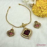 Gold jewelry set with maroon stones on a textured white surface with flowers.