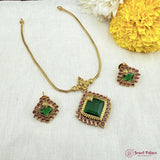 Gold necklace with green and purple gemstones on a white fabric background with yellow flowers.