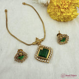 Gold necklace with green gemstones and matching earrings on a textured surface with yellow flowers.