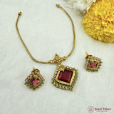 Gold necklace with red gemstone and matching earrings on a light background with flowers.