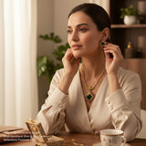 Woman wearing a necklace and earrings, sitting at a table with a cup and jewelry box.