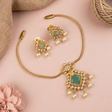 Gold-toned jewelry set with a necklace, earrings, and a decorative pendant, arranged on a soft pink background with burlap and a pink flower prop.