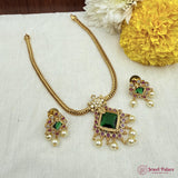 Gold necklace with green and red gemstones on a white fabric background with yellow flowers.