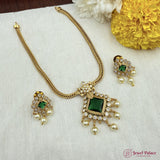 Gold necklace with green gemstones and matching earrings on a white fabric background with flowers.