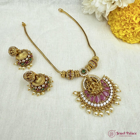 Gold necklace with pink stones and matching earrings on a white fabric background with flowers.