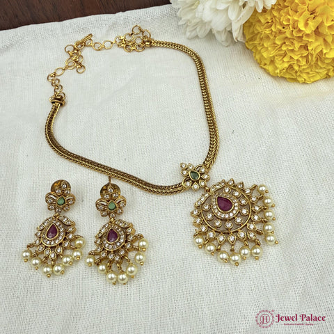 Gold necklace and earrings set with maroon and green stones on a white fabric background.