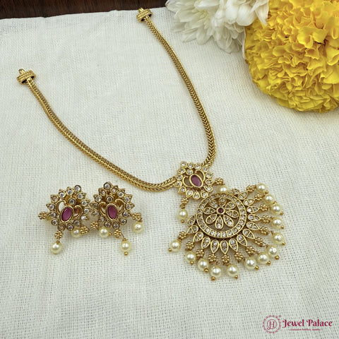 Gold necklace and earrings set with pearls and red stones on a white fabric background with yellow flowers.
