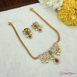 Gold necklace with pearls and gemstones on a white fabric background with flowers.