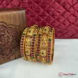 Gold bangles with gemstones on a white surface with a red quilted background