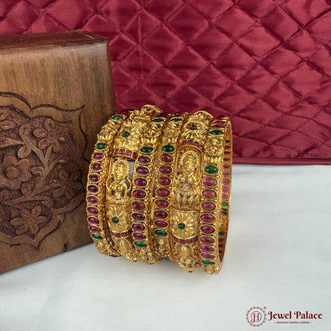 Gold bangles with gemstones on a white surface with a red quilted background