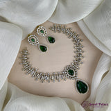 Jewelry set with necklace and earrings on a white fabric background, featuring green gemstones and silver accents.
