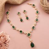 Gold jewelry set with emerald green stones and white crystal accents, including a necklace, matching earrings, and a bracelet, arranged on a pink background with decorative burlap and a rose.