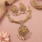 Gold-toned traditional jewelry set with a necklace, earrings, and pendant featuring pink stone drops and white faux pearls, arranged on a soft pink background with burlap and a flower prop.