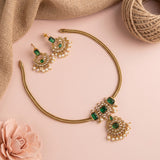 Gold-plated Indian traditional jewelry set featuring a necklace and matching earrings with green rectangular stones and white pearl accents, styled on a pink background with burlap and a pink rose.