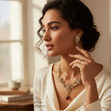 Woman wearing a gold necklace and earrings in a softly lit room.