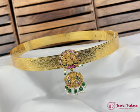 Gold belt with intricate designs and gemstones on a white cushion with wooden background