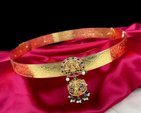Gold belt with intricate designs and colorful stones on a red fabric background
