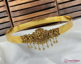 Gold belt with intricate designs and dangling elements on a white fabric background.