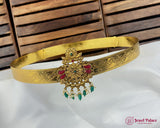 Gold belt with intricate designs and gemstones against a wooden background