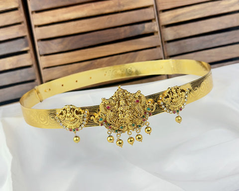 Gold belt with intricate designs and small beads on a white surface with wooden background