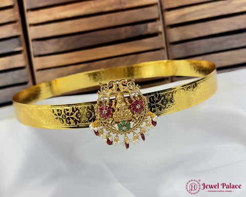 Gold bracelet with intricate design and gemstones on a white surface with wooden background