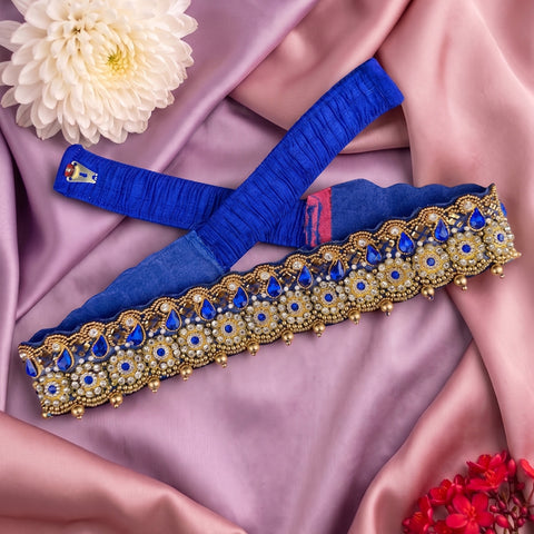 A royal blue fabric waist belt or sash with ornate gold and blue beaded embroidery, laid flat on a pink satin fabric background with decorative flowers.