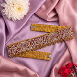 A decorative waist belt with intricate beadwork and embroidery, laid out on draped pink satin fabric with decorative flowers.