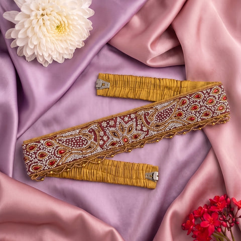 A decorative waist belt with intricate beadwork and embroidery, laid out on draped pink satin fabric with decorative flowers.