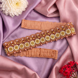 A decorative embroidered waistband or belt laid flat on draped pink satin fabric, with floral and bead embellishments in gold, white, and pink. Two matching fabric bands are visible, styled with flowers in the corners.