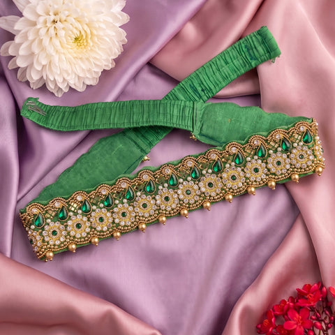 A green fabric garment accessory with ornate gold and green beaded embroidery, laid flat on draped pink satin fabric with decorative flowers.