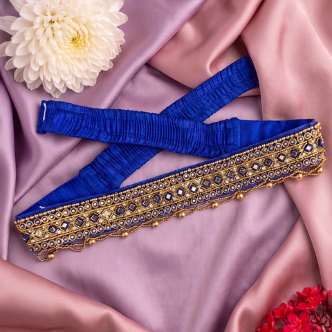 A royal blue blouse border with intricate gold and silver mirror work embroidery, laid out on draped pink satin fabric with decorative white and red flowers.